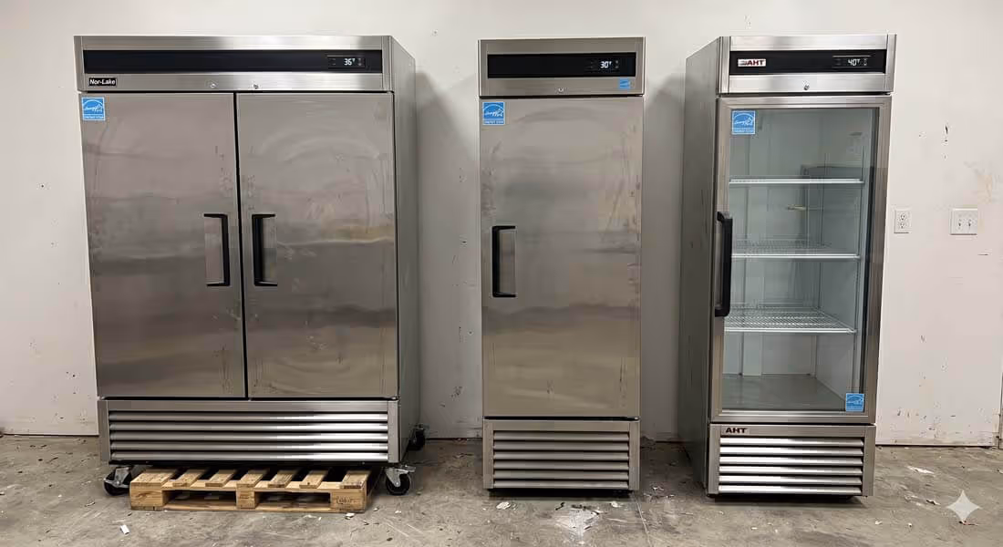 Three commercial stainless steel refrigerators against a white wall, one with double doors, one single door, and one single glass door with shelves.