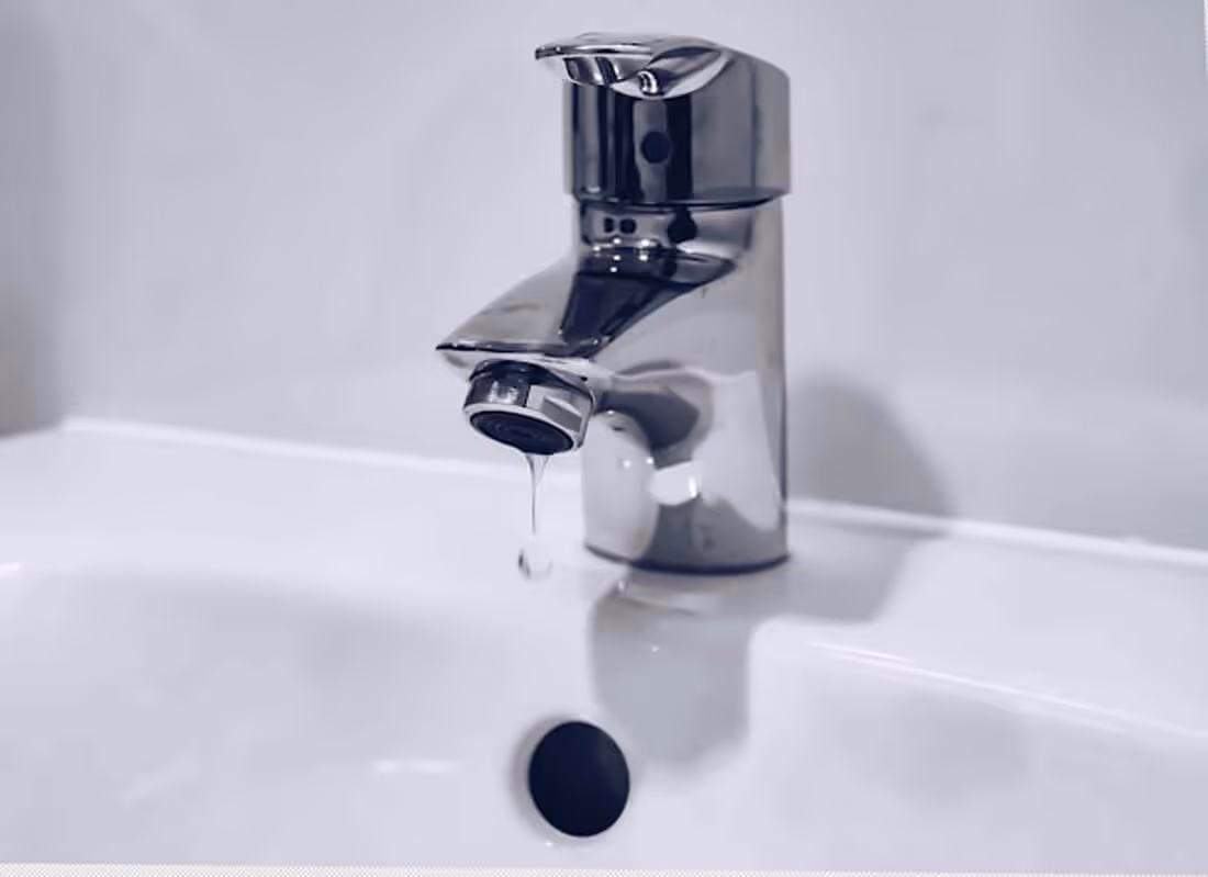 Close-up of a chrome faucet with a drop of water dripping into a white sink.